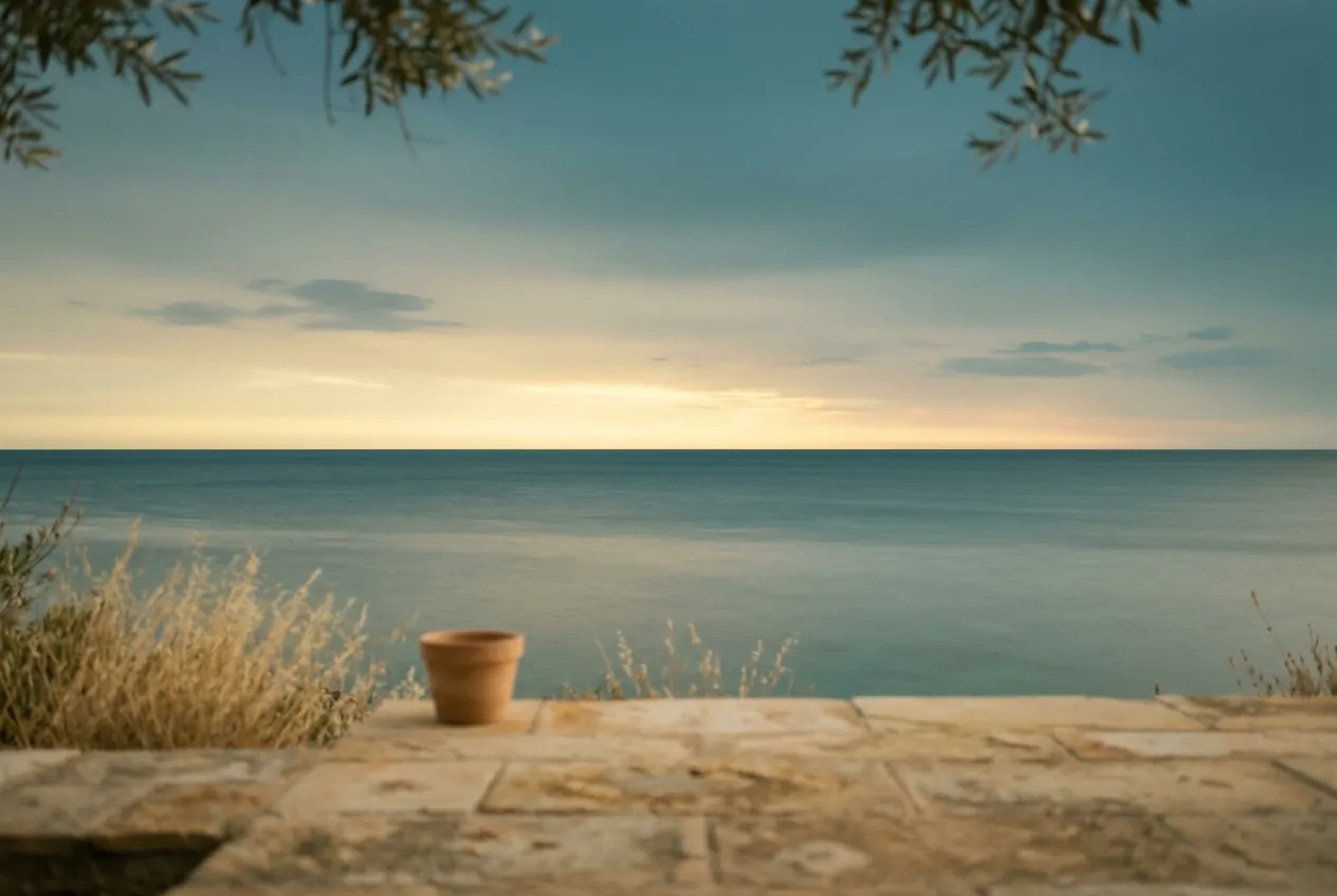 A stone terrace above a calm sea at dusk, olive branches at the top of the frame.