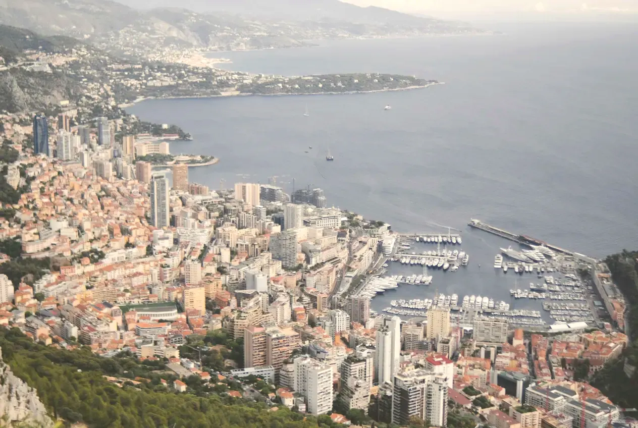 Monaco seen from the hills above: the city pressed along the coast, the harbour, and the bay beyond.