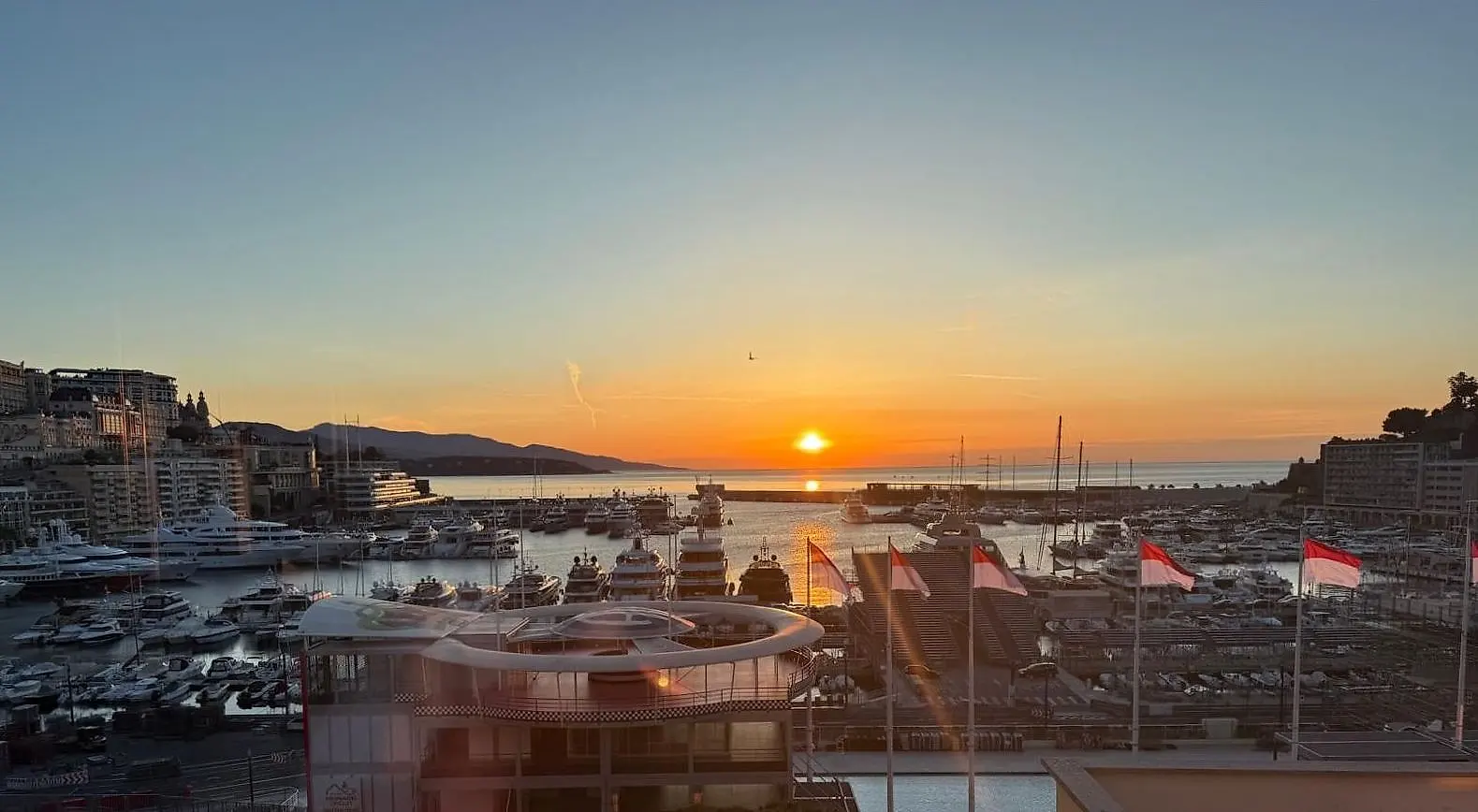 The sun setting into the sea beyond the harbour, flags along the quay in the last light.