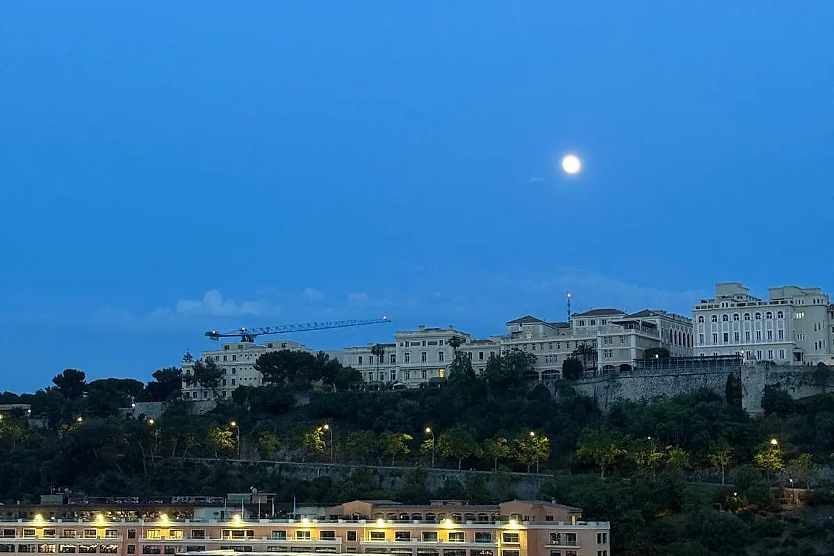 The Rock of Monaco at dusk under a rising moon, the old town along the top of the cliff.
